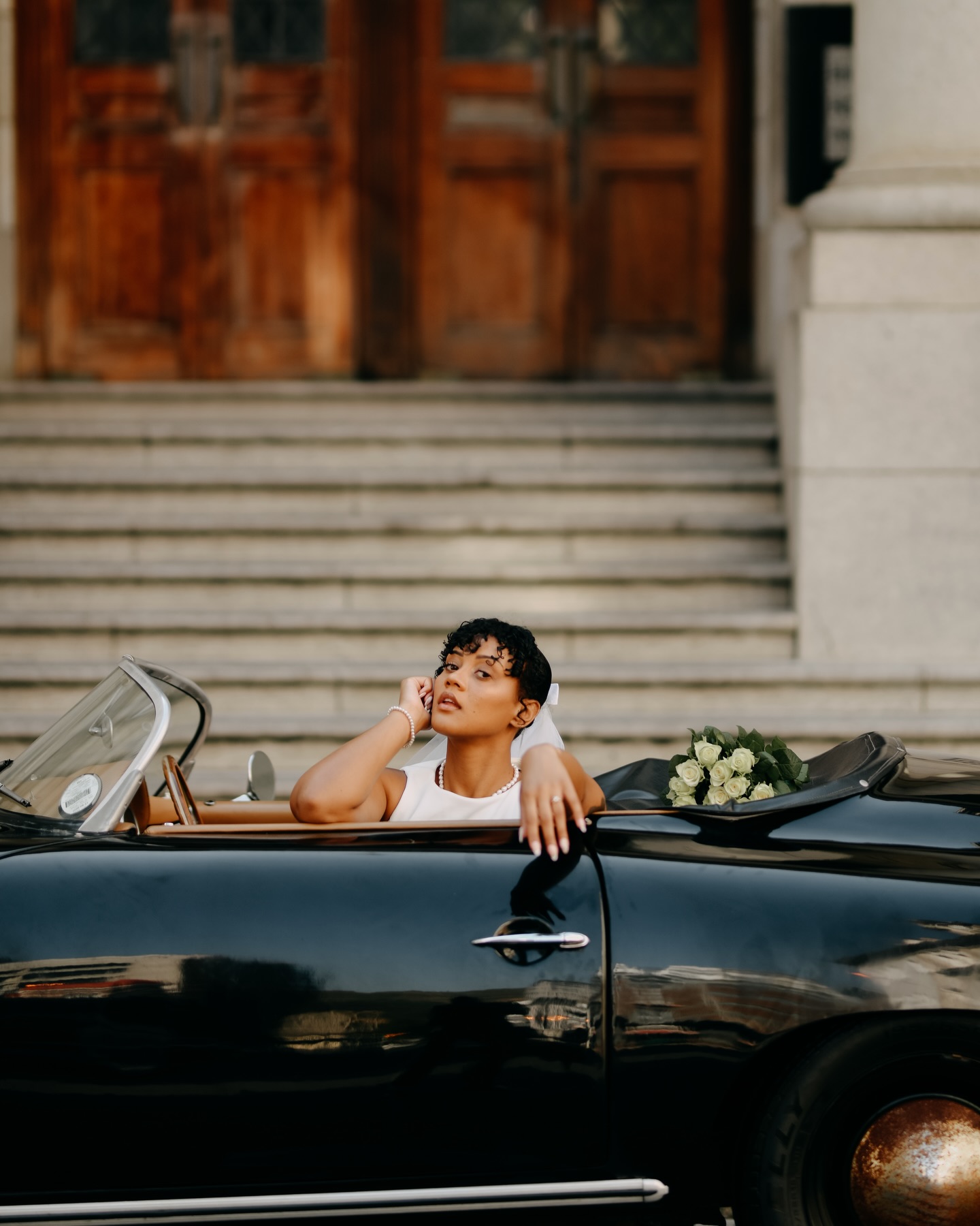 Bride seated in the black Speedster with a bouquet behind her